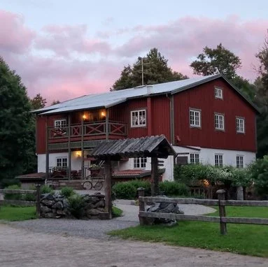 Herrtorps Qvarn & Öringen omgivet av grönska, grusgång och träd i skymningens ljus.