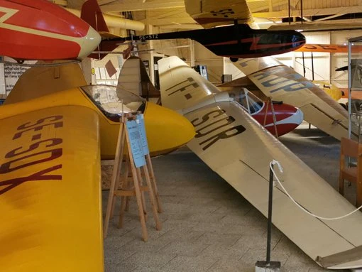 Flera klassiska segelflygplan uppställda i rad i en hangar på Ållebergs Segelflygmuseum