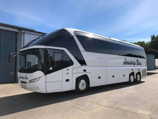 En stor, vit turistbuss från Stenstorps Buss parkerad utomhus under en klarblå himmel.