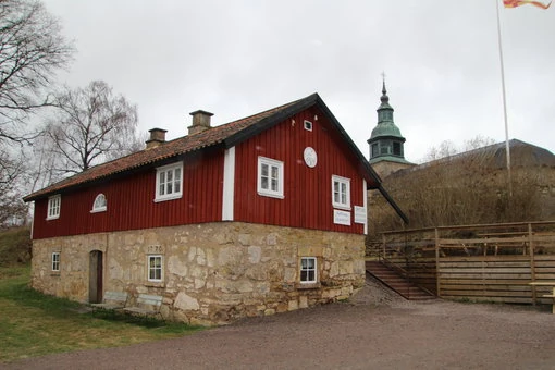 En vacker röd byggnad med vita knutar och stenfundament, belägen vid Gudhems kyrka.