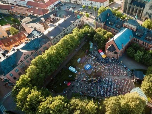 Flygbild över Skara med en stor samling människor på torget, omgivna av historiska byggnader. Handla i Skara