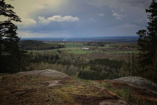 Vy från Mössebergs fornborg över ett vidsträckt landskap med skogar, fält och en dramatisk himmel.