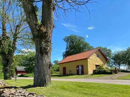 Gult hus med rött tak omgivet av grönska och stora träd vid Gudhems klostermuseum.